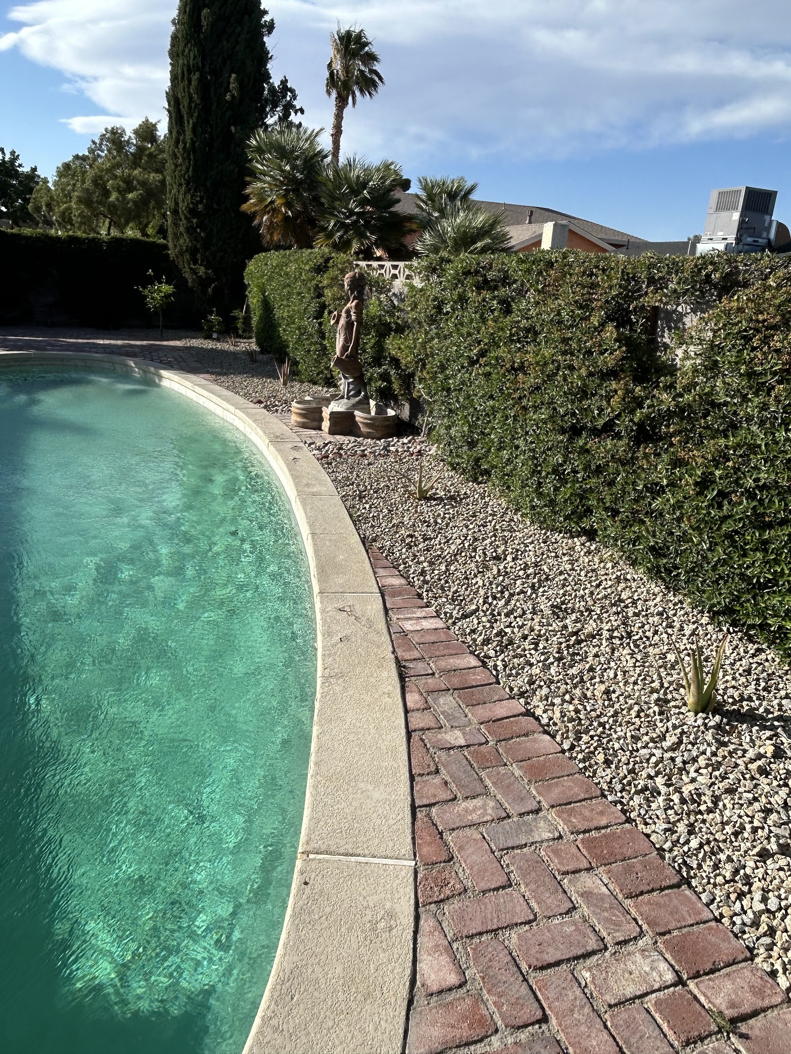 Backyard pool with brick paver walkway, gravel landscaping and statue fountain