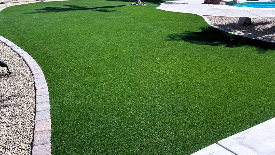 Lush artificial turf lawn with paver border beside pool and gravel bed